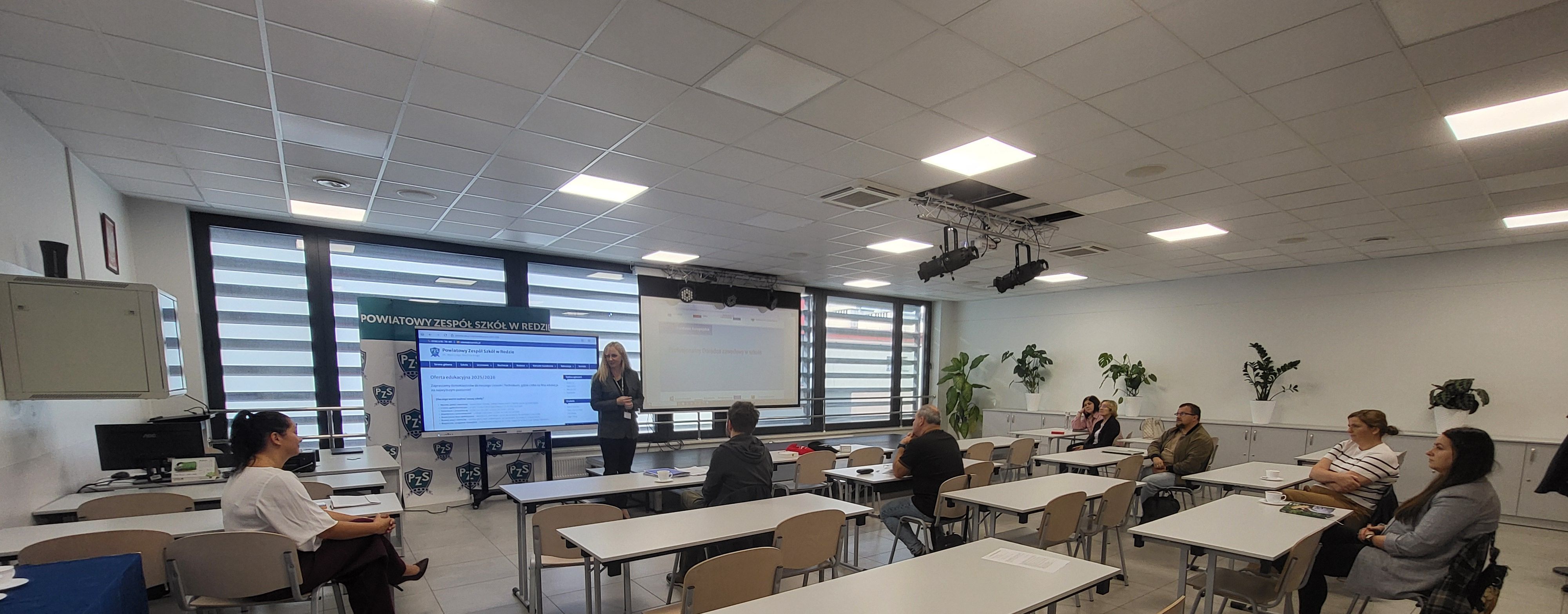 Widok na salę wykładową z wyświetlaną prezentacją.